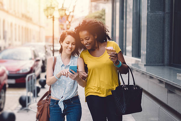 City girls on a leisure walk Smiling girls walking at the street and using smartphone street friends stock pictures, royalty-free photos & images