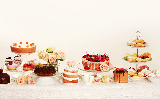 Table with loads of cupcakes, cake pops, birthday cakes, flowers and fruits. Light background 