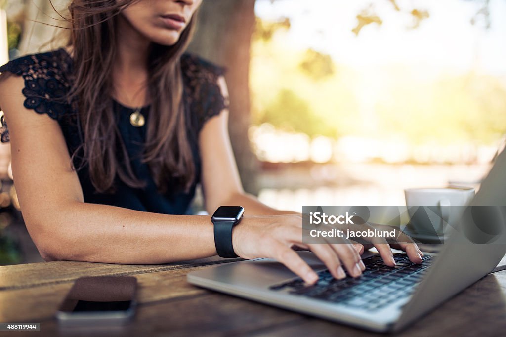 Woman working on laptop in a cafe Young woman wearing smartwatch using laptop computer. Female working on laptop in an outdoor cafe. Smart Watch Stock Photo