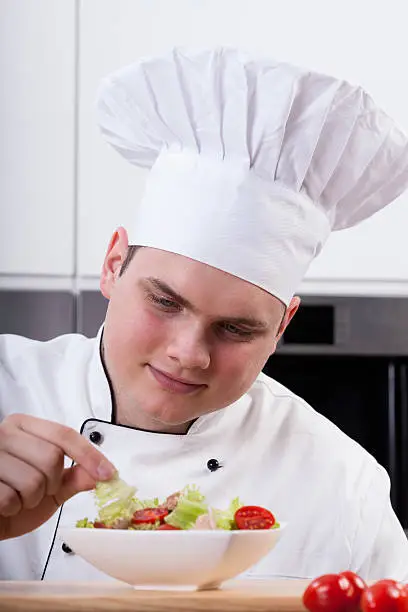 Young chef decorating delicious salad in kitchen
