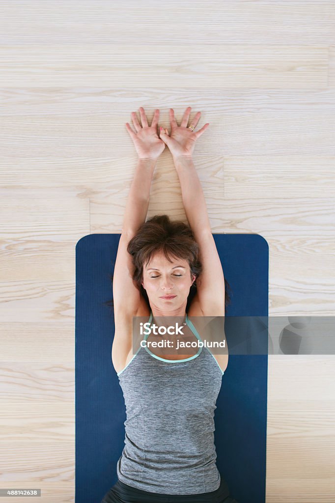 Fitness woman exercising on yoga mat Top view of woman lying on floor with her eyes closed and stretched arms. Fitness woman exercising on yoga mat. Yoga Stock Photo
