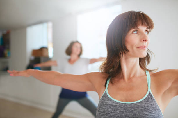 Woman doing the warrior pose during yoga class Portrait of beautiful young woman doing the warrior pose during yoga class. Yoga instructor performing Virabhadrasana position in gym. warrior 2 stock pictures, royalty-free photos & images