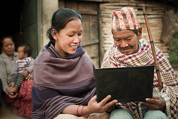 Rural Asian young woman showing laptop to a senior man. Outdoor day time close-up image under natural light of a rural Asian family with a Laptop. Young happy woman showing laptop computer to her grandfather, her mother-in-law and son is in the background. Horizontal composition with selective focus. central asian ethnicity photos stock pictures, royalty-free photos & images