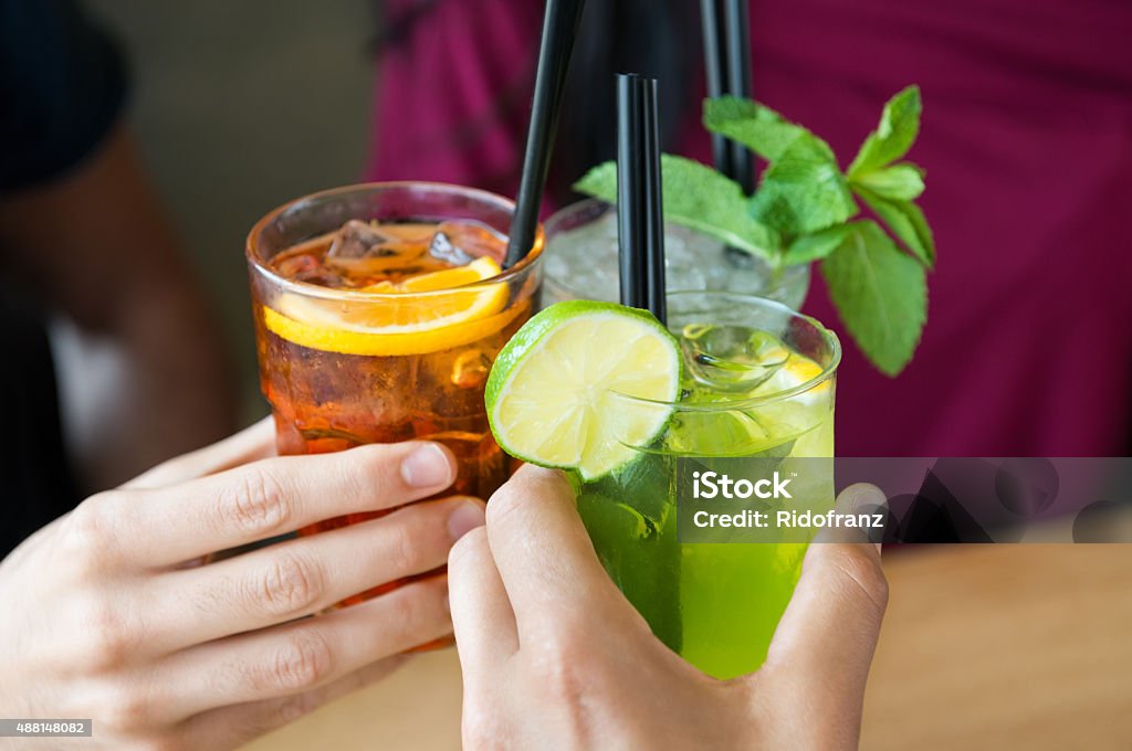 Aperitif with friends Closeup shot of friends toasting with cocktails. Young people drinking at aperitif. Shallow depth of field with focus on friends hand toasting juice glass. Close up of hands holding a cocktail glass. Cocktail Stock Photo