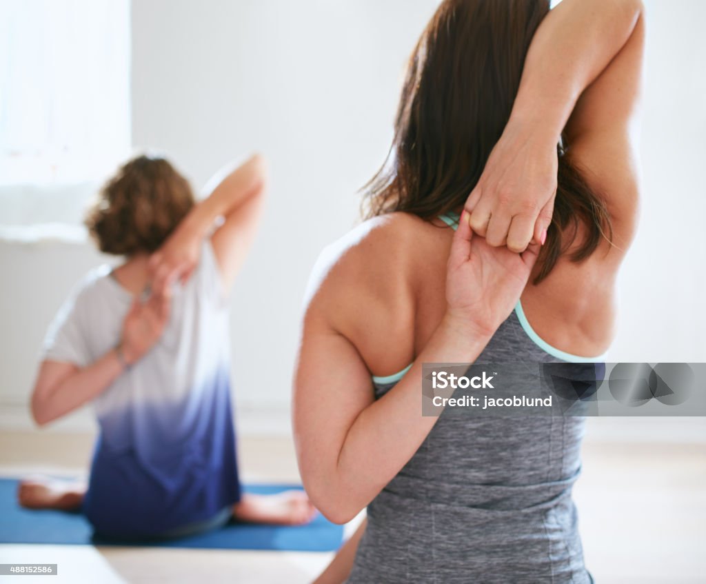 Women practicing gomukhasana in yoga class Rear view of women practicing gomukhasana in yoga class. Fitness females holding hands behind their back and stretching. Triceps and shoulders exercise. Cow Face Pose Stock Photo