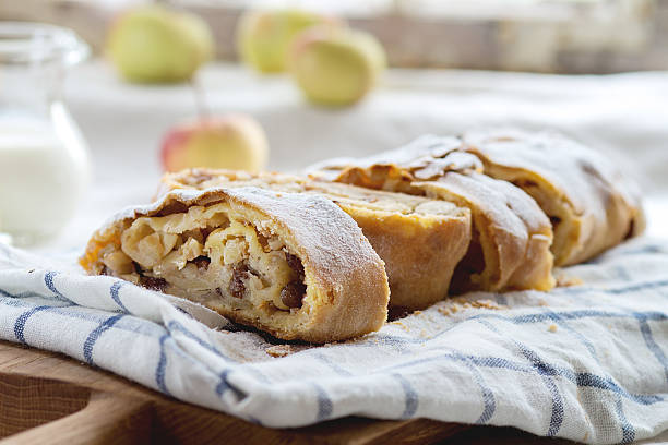 Apple strudel Sliced fresh baked homemade apple strudel over towel on kitchen table with jug of milk and apples. Rustic style. Natural day light. apple strudel stock pictures, royalty-free photos & images