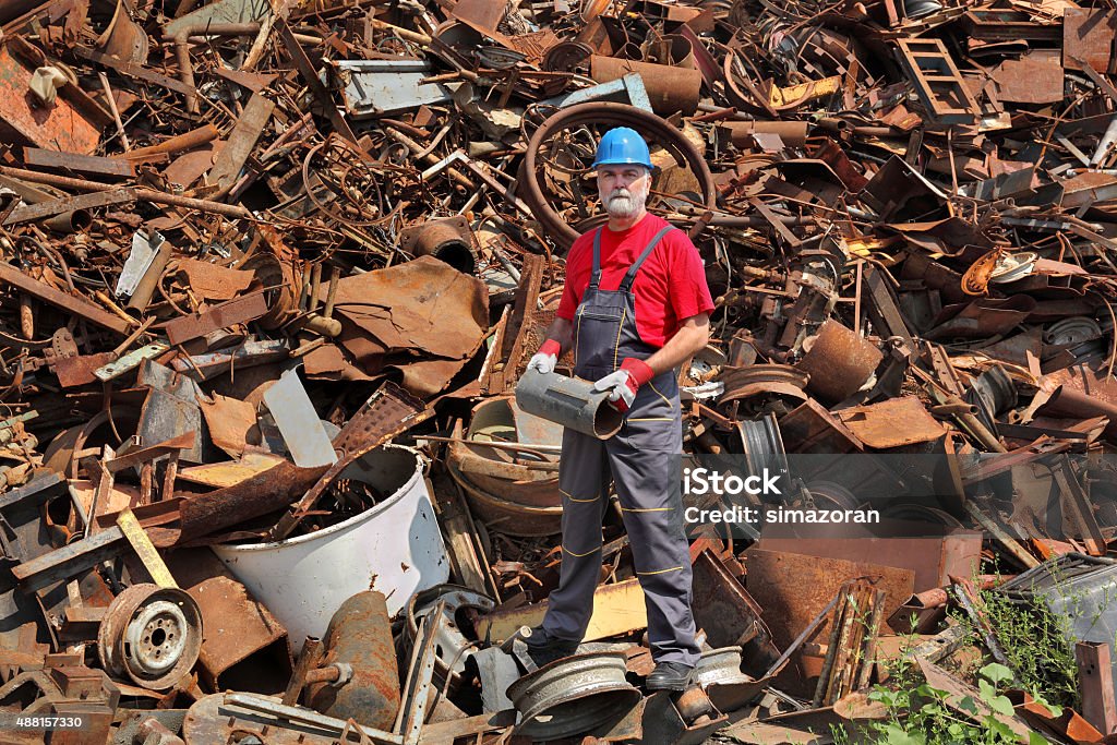Recycling industry, worker stand at heap of old metal Worker hold tube at heap of scrap metal ready for recycling Junkyard Stock Photo