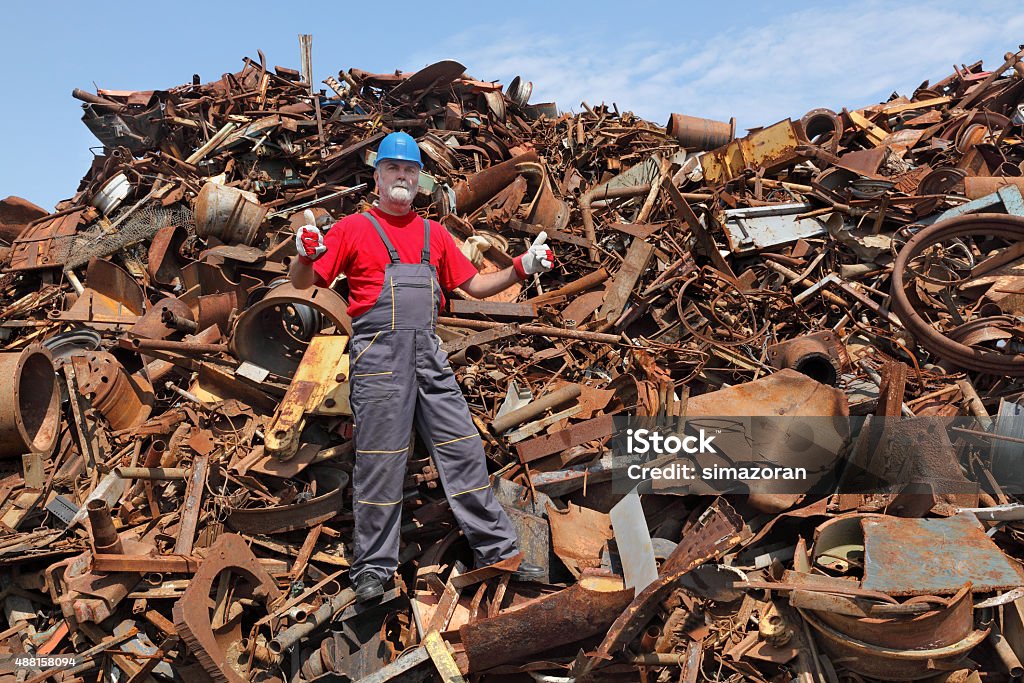 Recycling industry, worker gesture at heap of old metal Worker gesturing at heap of scrap metal ready for recycling, thumbs up Junkyard Stock Photo