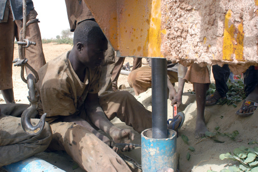 Liguidimalgem, Burkina Faso - February 24, 2007: In Africa water is in-depth, it is necessary to make a drilling. Two blue-collar workers tighten an extension for the head of drilling