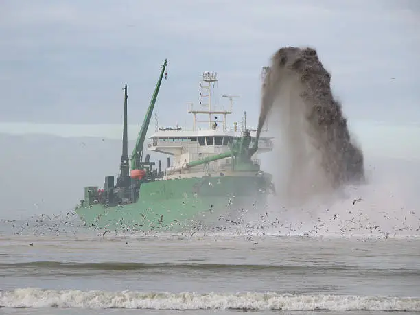 Dredger vessel pumping sand onto the coastline to gain new land from the sea creating a port.