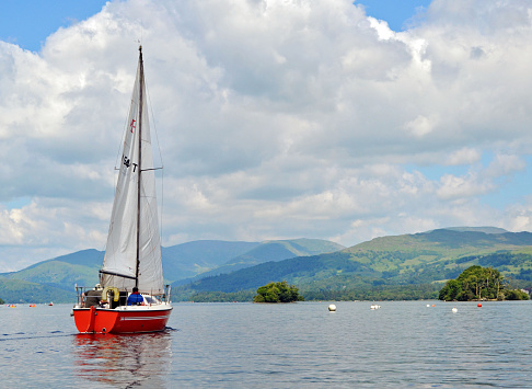 Windermere, England - June 18, 2014: People sailing and enjoying the scenery onboard a sailing boat on lake Windermere, in the heart of the Lake District. Other people can be seen conoeing in the far,