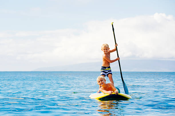 Boys Having Fun Stand Up Paddling Young Boys Having Fun Stand Up Paddling Together in the Ocean paddleboard surfing oar water sport stock pictures, royalty-free photos & images