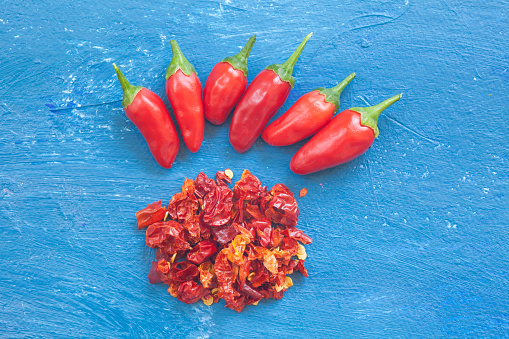 A view red peppers laying on  blue background. Aranged in a row with milled chilli pieces.
