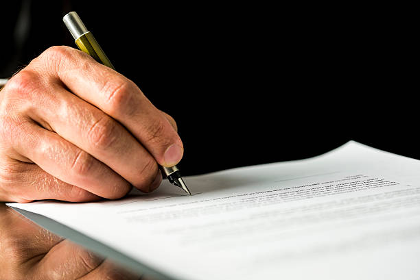 Male hand signing a contract, employment papers, legal document Closeup of male hand signing a contract, employment papers, legal document or testament. Isolated over black background. petition stock pictures, royalty-free photos & images