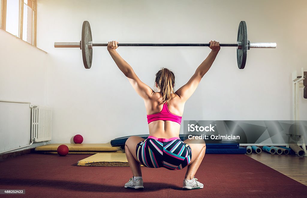 Girl doing squats with weight Young adult girl doing heavy duty  squats in gym with barbell Above Stock Photo