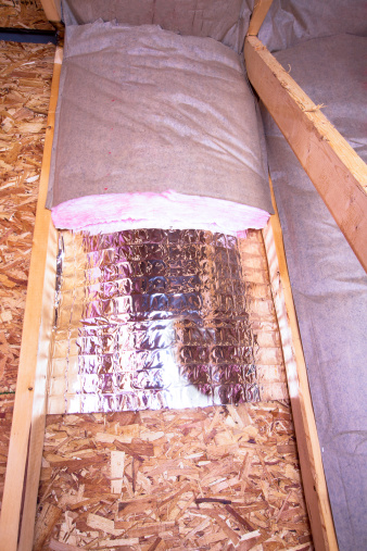 Insulation of attic with fiberglass cold barrier and reflective heat barrier between the attic joists, work is ongoing