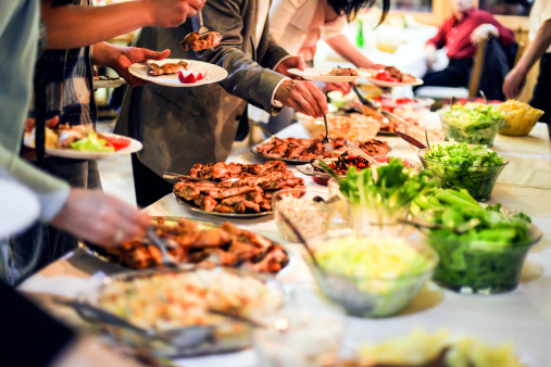 Large group of people picking food (grilled meat and salads) from a buffet table. Unrecognizable Caucasian adults, both female and male.