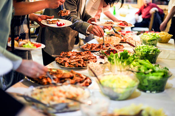 People eating Large group of people picking food (grilled meat and salads) from a buffet table. Unrecognizable Caucasian adults, both female and male. people banque stock pictures, royalty-free photos & images