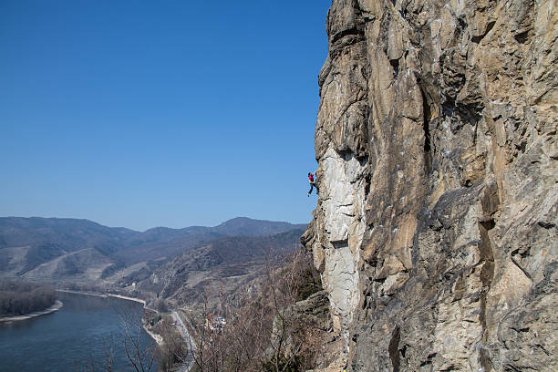 Female rock climber  is climbing a difficult route in Dürnstein Wachau Austria along a vertical rock wall. Danube in the background. Plenty of copy space.