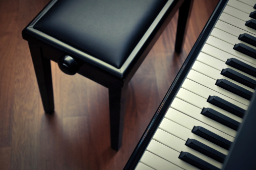 Top diagonal view of piano keyboard and stool on a parquet floor.