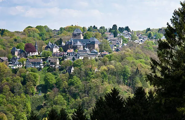 View on Schloss Burg and deciduous forest with coniferous trees in right foreground. The fortress, located in Solingen at river Wupper, is the largest reconstructed castle in North Rhine Westphalia, Germany and a popular tourist attraction.