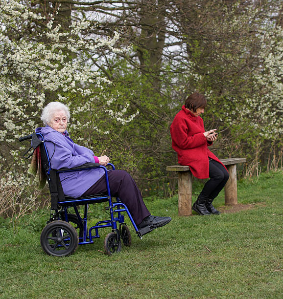 пожилые женщина, сидя в кресле-коляске рядом с молодой женщины. - senior women senior adult bench flower стоковые фото и изображения