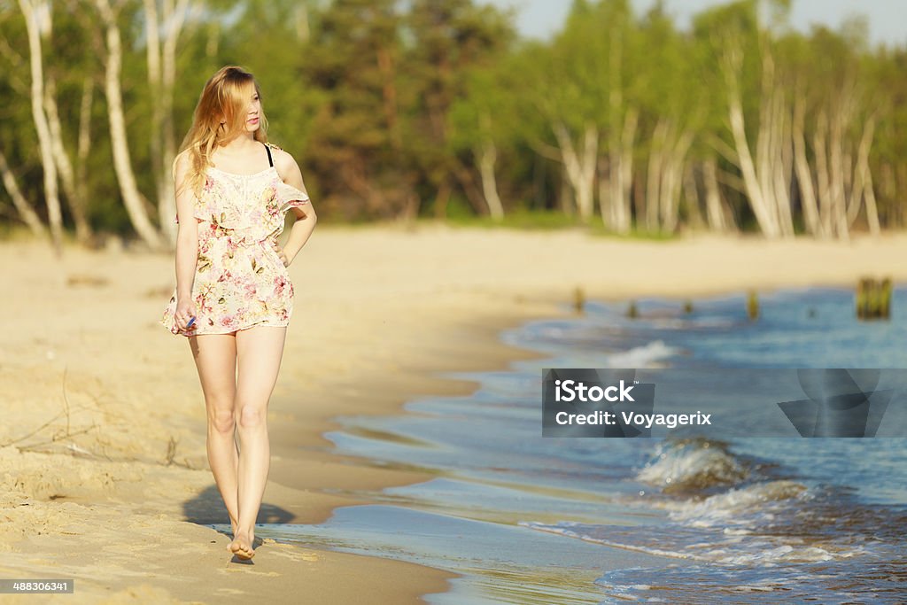 Summer vacation. Girl walking alone on the beach. Vacation. Girl in summer dress walking alone on the empty beach. Young woman relaxing on the sea coast. Summertime. Adult Stock Photo