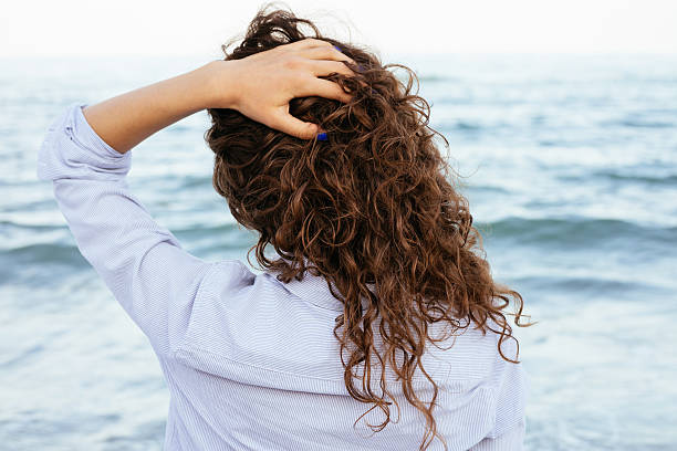 junge frau in shirt mit blick auf das meer - women long hair rear view beauty stock-fotos und bilder