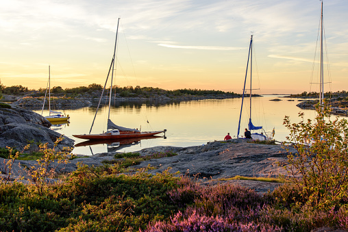 Sunset light over sailboats moored at small rocky island in the outer part of the archipelago. Old wooden sailboat in focus. Stockholm, Sweden.