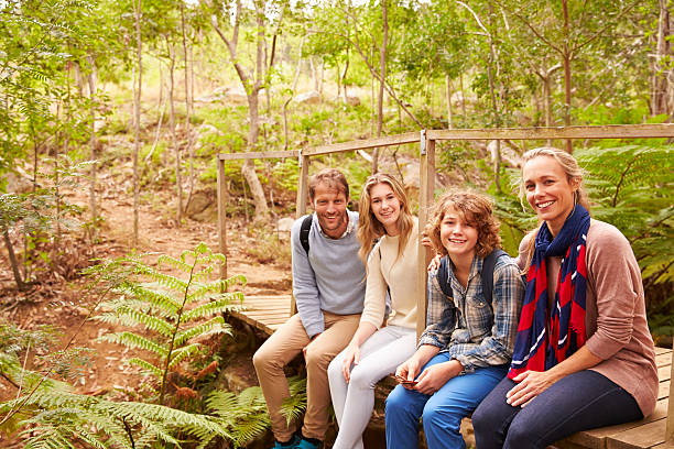 istock Family sitting on a bridge in Forest, looking to camera 488315884