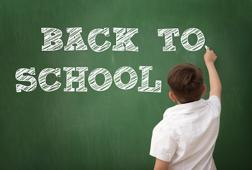 Schoolboy drawing BACK TO SCHOOL on blackboard, education concept