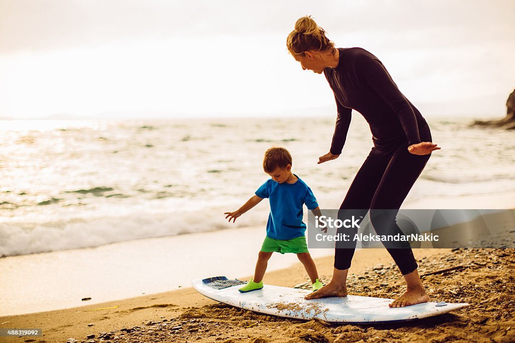 Surfing lessons Photo of a little surfer boy and his mother (his instructor) having a surfing class on the beach by the ocean Surfing Stock Photo