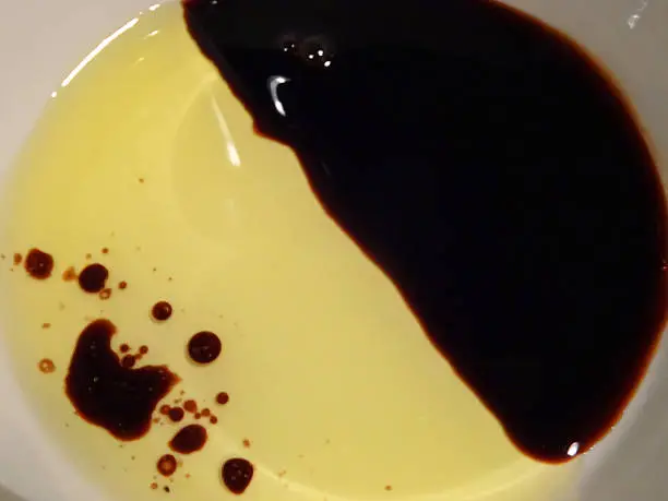 Photo showing a 'yin and yang' mixture of olive oil and balsamic vinegar, in a round white dish.