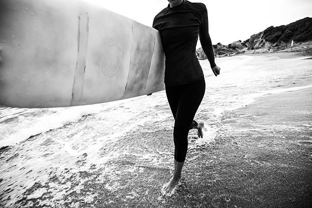 Photo of a surfer girl running to catch a good wave, holding her surfboard under the armpit