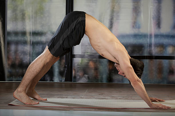 istock man doing yoga in office - dog facing downward 488350764