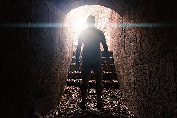 istock Man stands in dark stone tunnel with glowing end 488351220