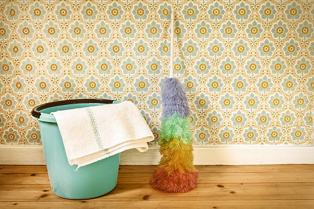 Sepia toned image of a feather broom and bucket in front of retro wallpaper