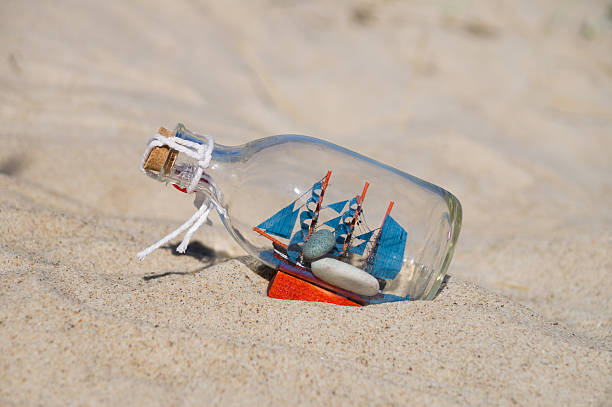 istock Small ship in the glass bottle lying in the sand 488354736