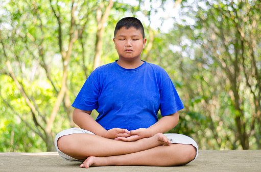 Young asian male teenager meditating in half lotus posture.