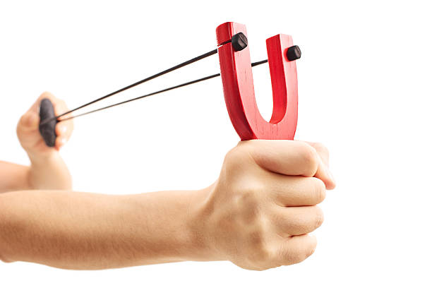 Hands holding a stretched slingshot isolated on white backgroun Hands holding a stretched slingshot with a rock in it isolated on white background rubber rocks stock pictures, royalty-free photos & images