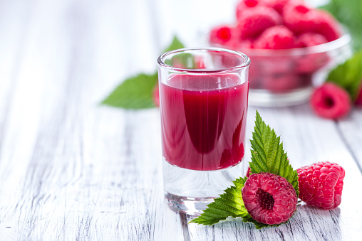 Glass with Raspberry Liqueur and fresh fruits on wooden background