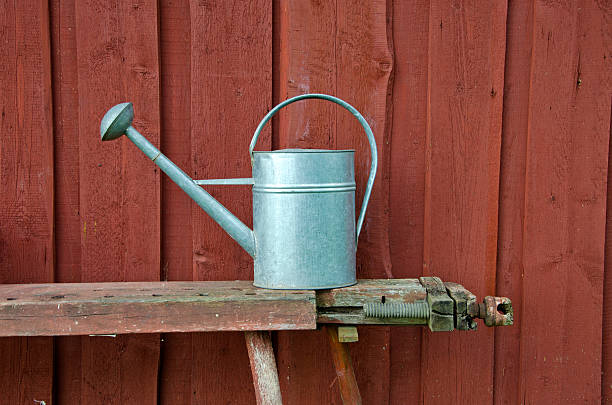 istock Metal watering can on bench besides red wooden wall 488362996