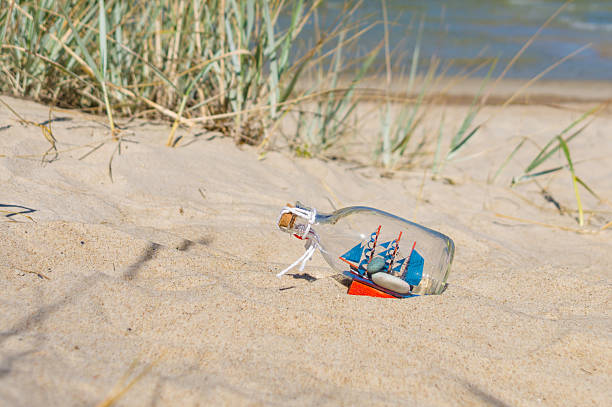 istock Small ship in the glass bottle lying on the beach 488364392