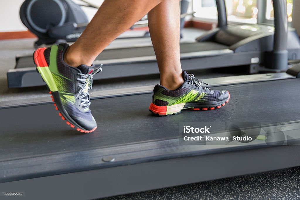 Close up man feet running on the treadmill Close up photos of man feet running on treadmill. He is wearing a sport shoes which has a multi color green, red and black. The man running inside a gym , in the afternoon. 2015 Stock Photo