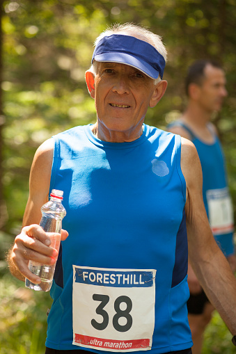 Portrait of a man wearing sun visor holding water bottle and smiling during ultramarathon race training