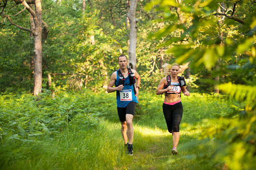 Male and female athletes running through forest trail during ultramarathon race.