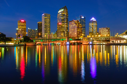 Photo of the Tampa Florida USA skyline and reflection in water at night with colorful streetlights.