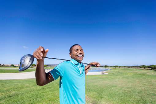 An african golfer smiling, holding his golf club over his shoulder with a big smile. Langebaan, Western Cape, South Africa.