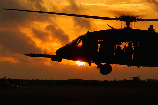 A black hawk helicopter of the US Marines, with soldiers inside, flying low at sunset.