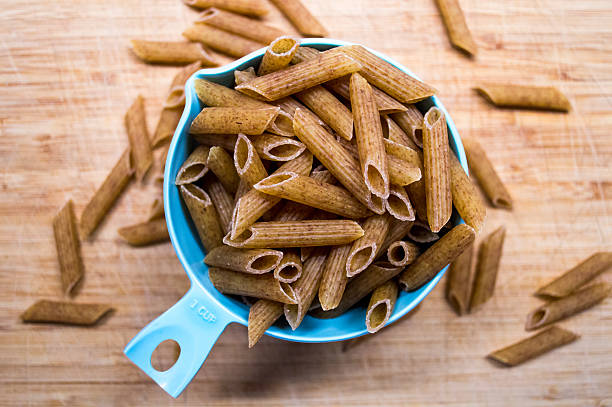 Brown Wholewheat/Wholemeal Dry Pasta Spilling Overhead View A one cup measurement of brown wholewheat penne pasta, a healthier and heartier alternative to the basic white penne pasta. whole wheat stock pictures, royalty-free photos & images